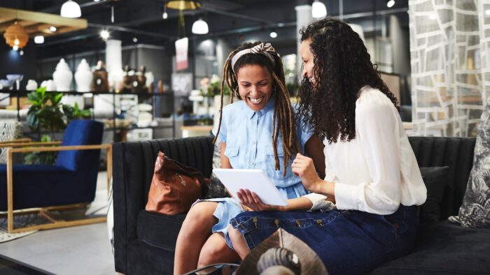 Two women in a furniture store smiling and looking at a table