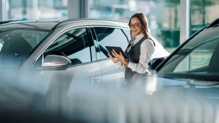 Photo of woman checking tablet between two SUVs in a car dealership