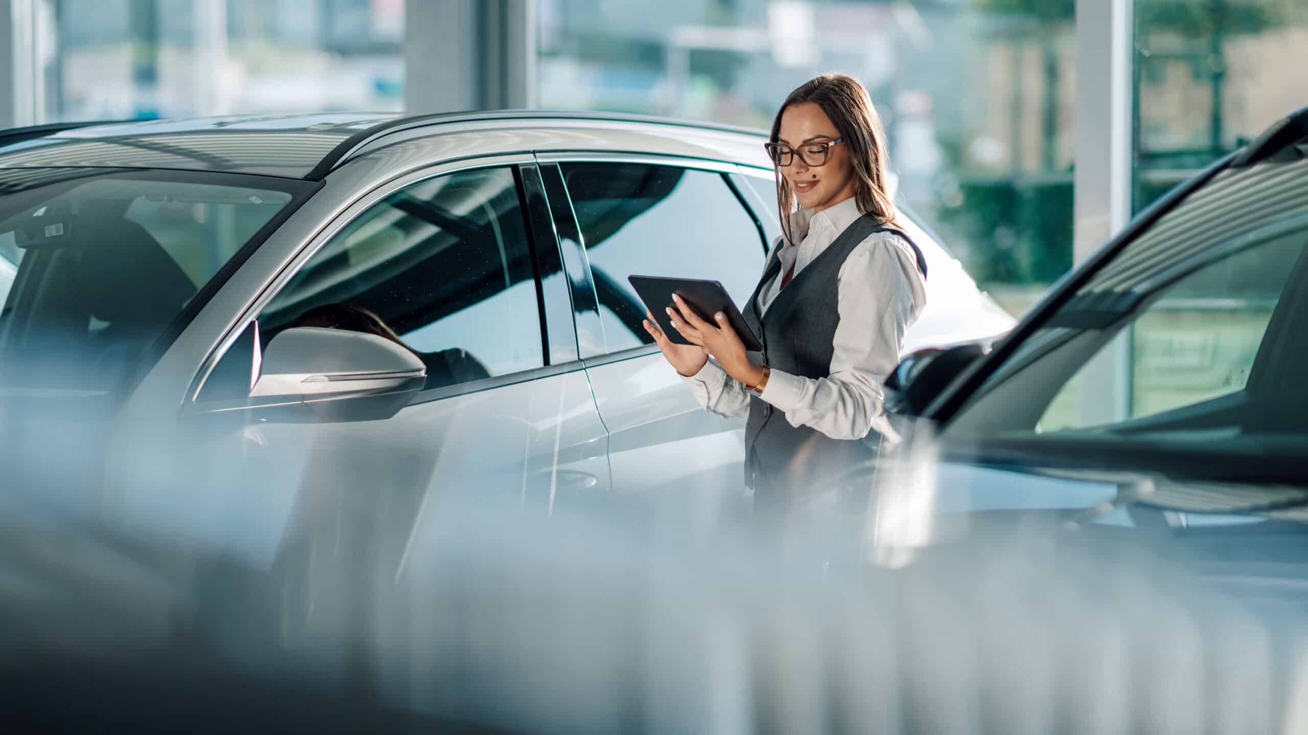 Photo of woman checking tablet between two SUVs in a car dealership