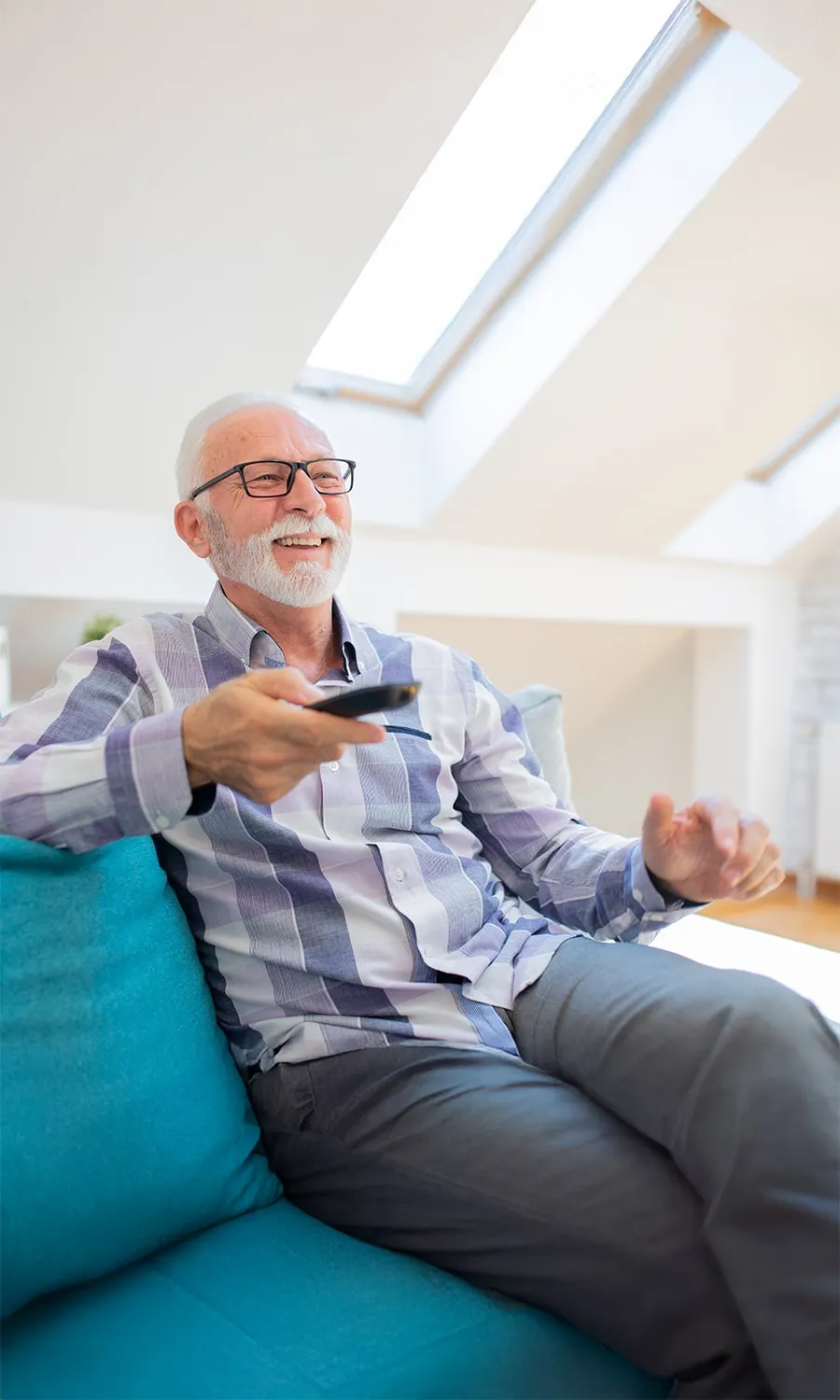 elderly man watching tv on a couch holding out a remote