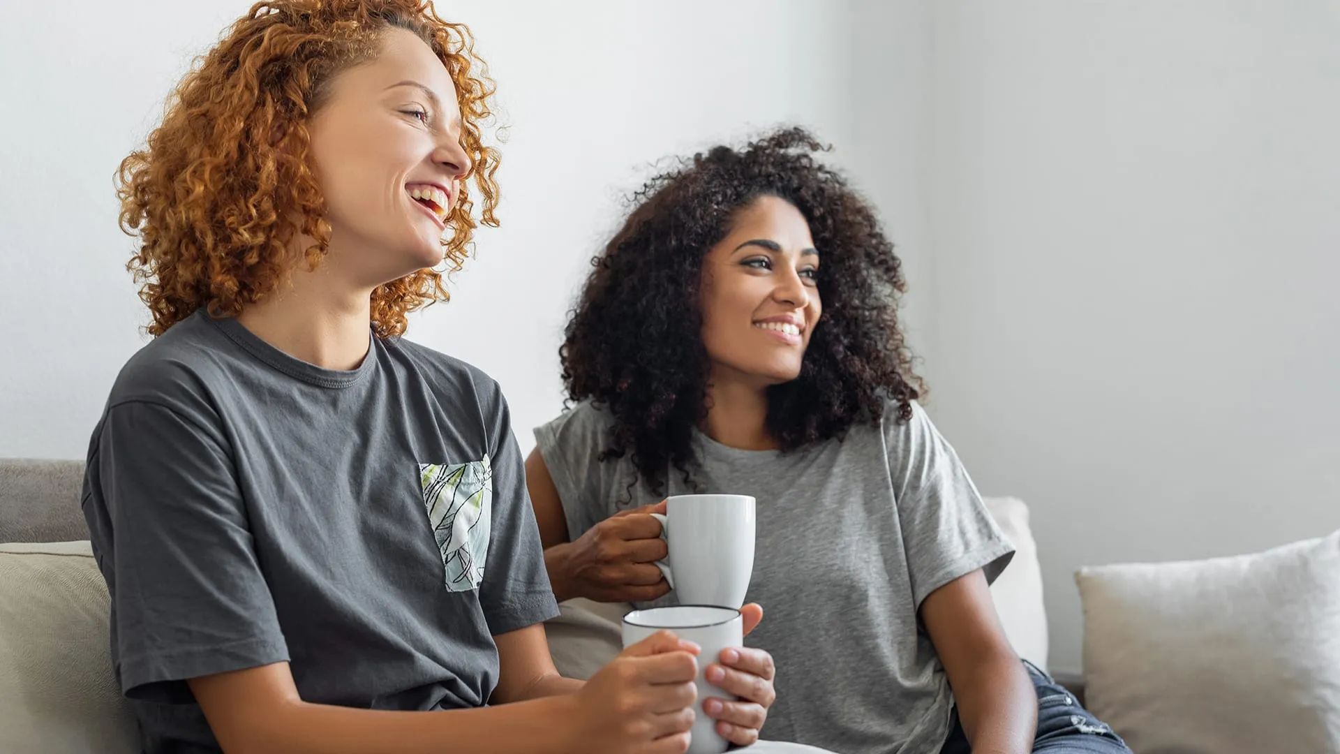 Two women with mugs sitting on the couch